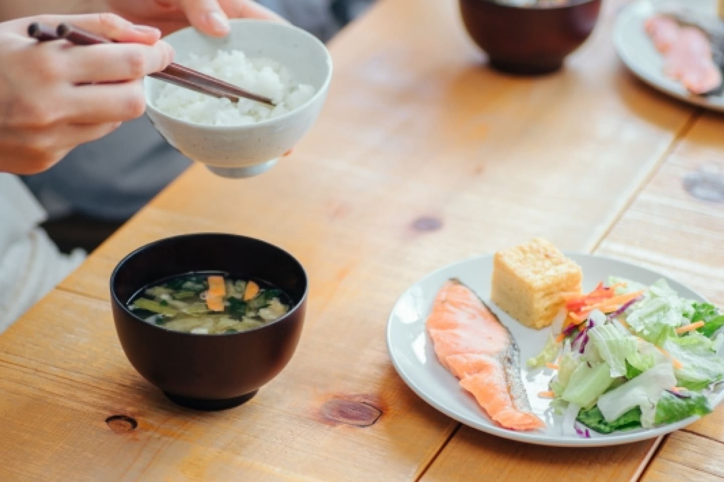 写真：ご飯、味噌汁、おかず。おかずのお皿には鮭、サラダ、卵焼きが載っている。